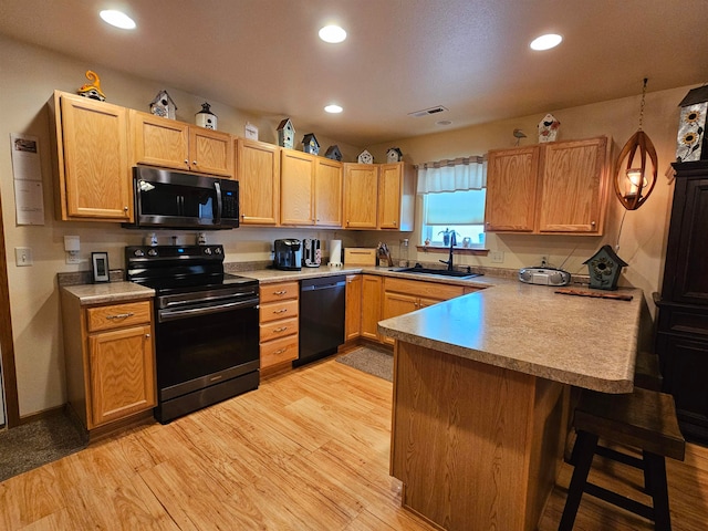 kitchen featuring light hardwood / wood-style flooring, black appliances, sink, kitchen peninsula, and a kitchen breakfast bar