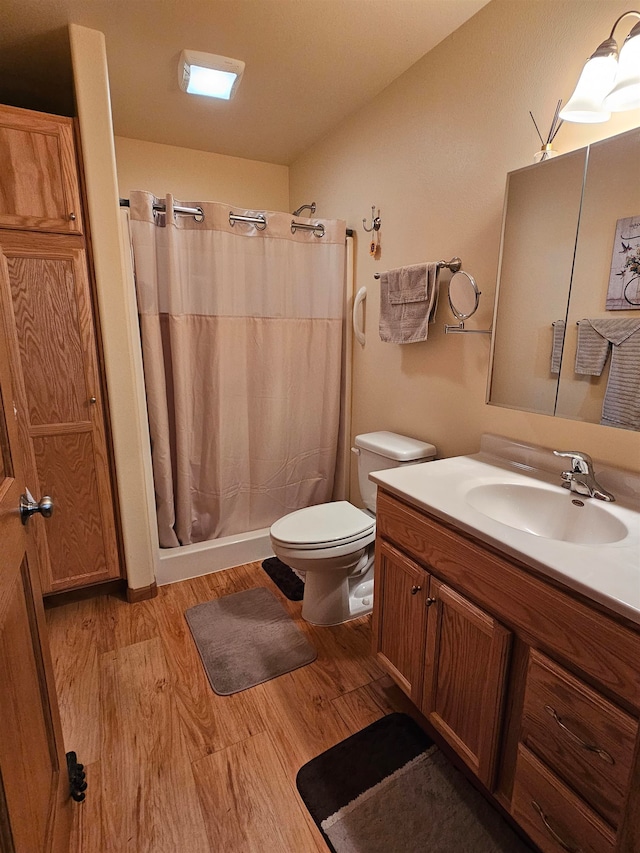 bathroom featuring hardwood / wood-style floors, walk in shower, toilet, and vanity