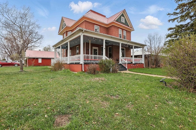 victorian-style house featuring brick siding, metal roof, a front yard, and covered porch