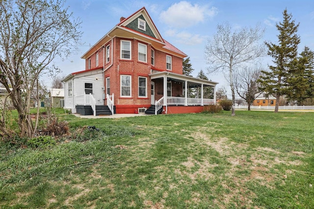 rear view of house with covered porch, brick siding, and a yard
