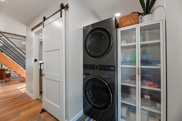 laundry room featuring a barn door, light hardwood / wood-style floors, and stacked washer / drying machine