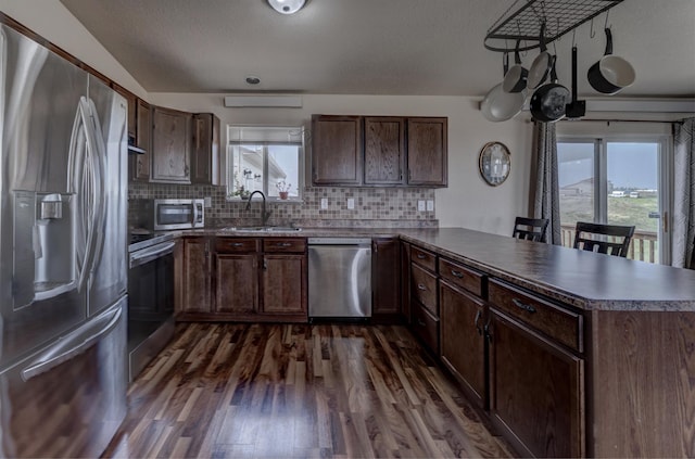 kitchen featuring sink, dark wood-type flooring, dark brown cabinets, stainless steel appliances, and kitchen peninsula