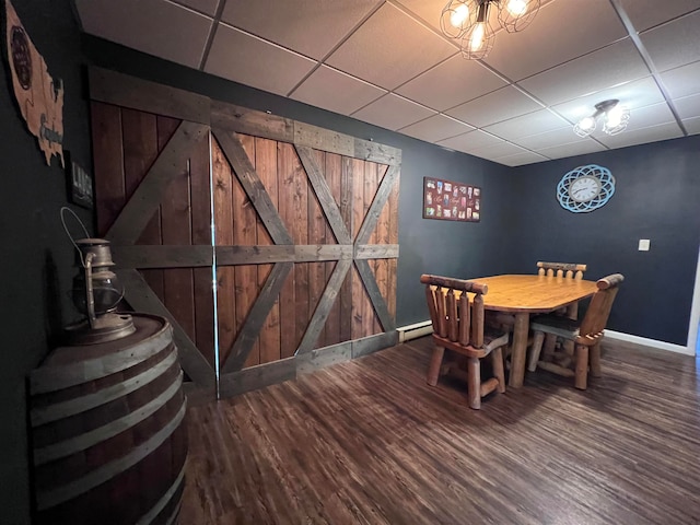 dining space featuring wooden walls, a baseboard heating unit, a barn door, hardwood / wood-style floors, and a paneled ceiling