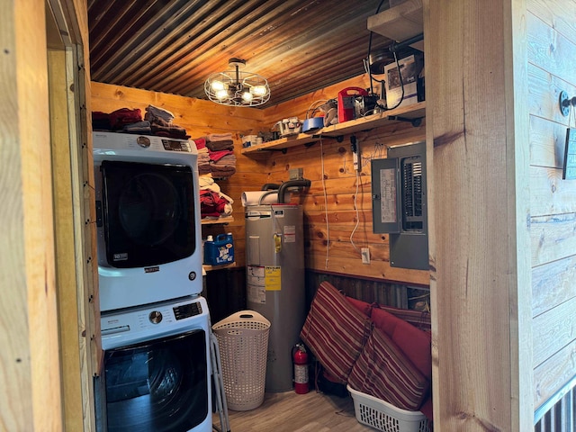 washroom with hardwood / wood-style floors, wood walls, stacked washer / drying machine, electric water heater, and an inviting chandelier