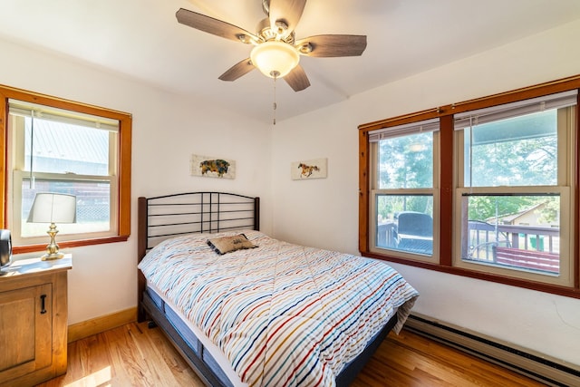 bedroom with light hardwood / wood-style floors, baseboard heating, multiple windows, and ceiling fan