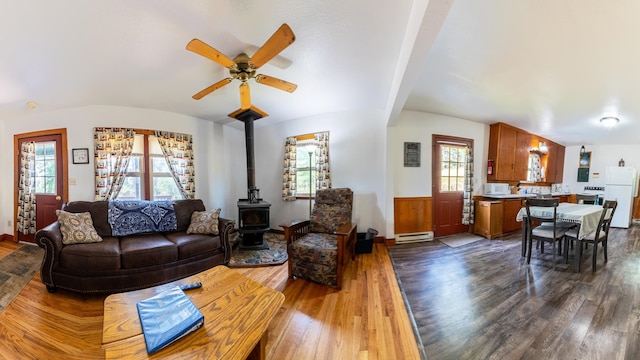 living room with a baseboard radiator, ceiling fan, hardwood / wood-style floors, and a wood stove