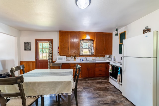 kitchen featuring light countertops, brown cabinets, dark wood-style floors, white appliances, and a sink