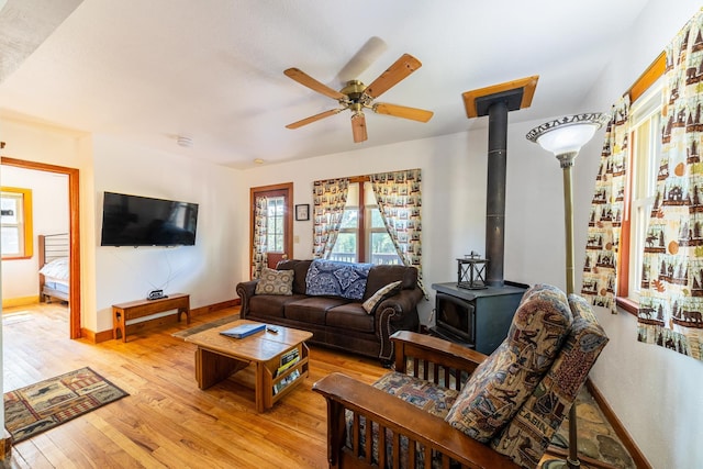 living room featuring ceiling fan, baseboards, a wood stove, and light wood-style floors