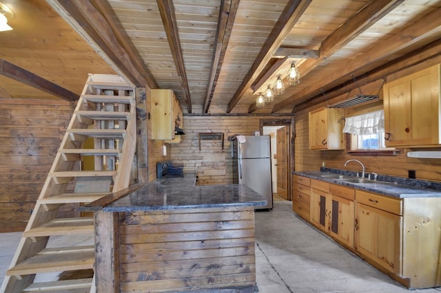 kitchen with stainless steel refrigerator, sink, beamed ceiling, wooden walls, and light brown cabinetry