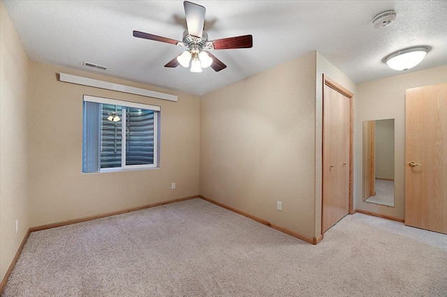 unfurnished room featuring ceiling fan, light colored carpet, and a textured ceiling