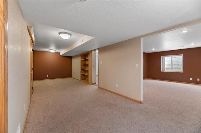 basement with built in shelves, light colored carpet, and a textured ceiling