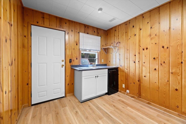 kitchen with wood walls, black dishwasher, white cabinetry, and light hardwood / wood-style flooring