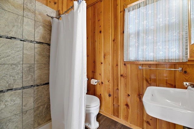 bathroom with wood-type flooring, wood walls, toilet, and sink