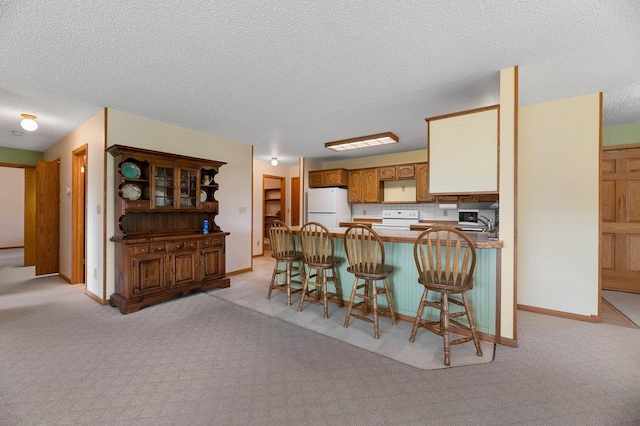 kitchen featuring white appliances, light colored carpet, a peninsula, and a kitchen bar