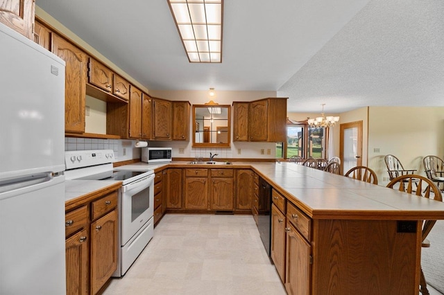 kitchen featuring light tile patterned flooring, a breakfast bar area, white appliances, an inviting chandelier, and decorative backsplash