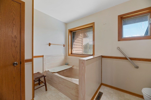 bathroom featuring tile patterned flooring, a bathing tub, toilet, and a wealth of natural light