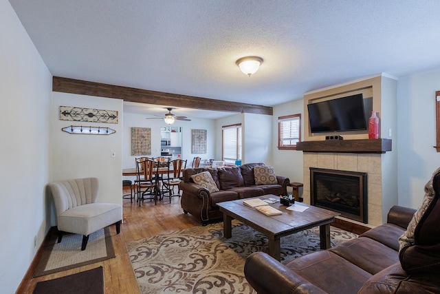 living room with a textured ceiling, a fireplace, light wood-type flooring, and ceiling fan