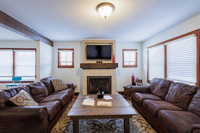 living room featuring beamed ceiling, a tile fireplace, and a textured ceiling