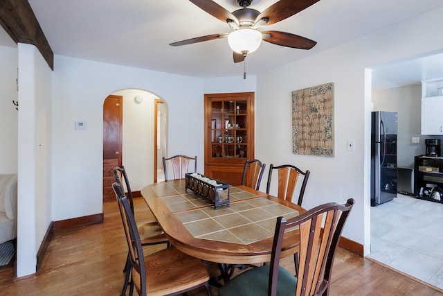 dining space with arched walkways, a ceiling fan, baseboards, and wood finished floors