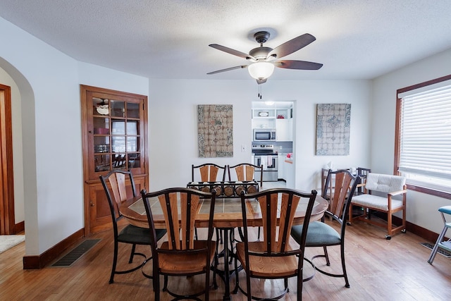 dining area with visible vents, baseboards, light wood-type flooring, arched walkways, and a textured ceiling