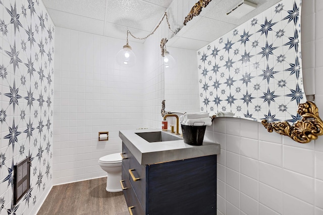 bathroom featuring a paneled ceiling, toilet, vanity, hardwood / wood-style floors, and tile walls