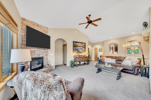 carpeted living area featuring arched walkways, lofted ceiling, ceiling fan, and a stone fireplace