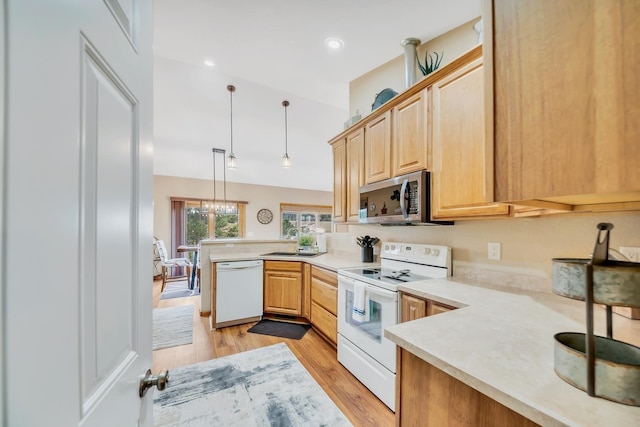 kitchen featuring light countertops, light brown cabinets, a sink, white appliances, and a peninsula