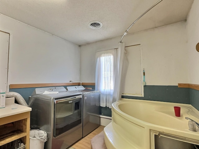 laundry area featuring light wood finished floors, a textured ceiling, laundry area, visible vents, and washer and dryer