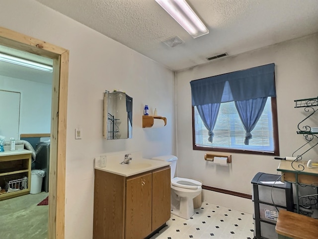 bathroom with toilet, vanity, a textured ceiling, baseboards, and visible vents