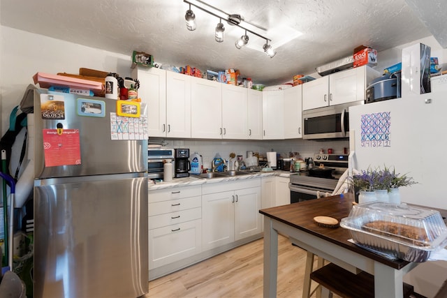 kitchen with light wood-type flooring, appliances with stainless steel finishes, rail lighting, a textured ceiling, and white cabinetry