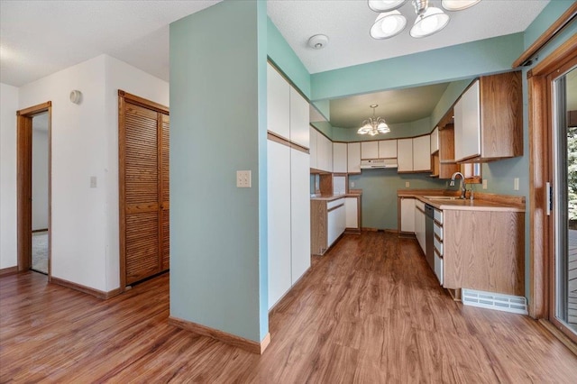 kitchen with light hardwood / wood-style flooring, decorative light fixtures, dishwasher, sink, and a notable chandelier