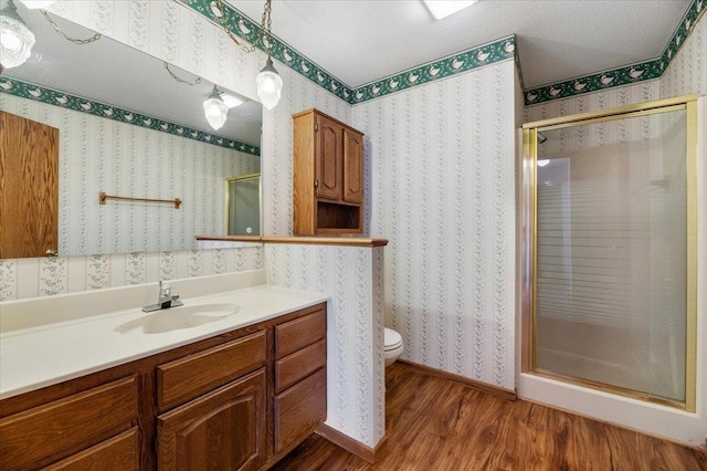 bathroom with wood-type flooring, a shower with shower door, vanity, and toilet