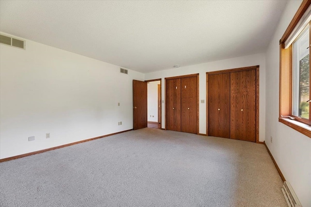 unfurnished bedroom with multiple closets, carpet floors, and a baseboard heating unit