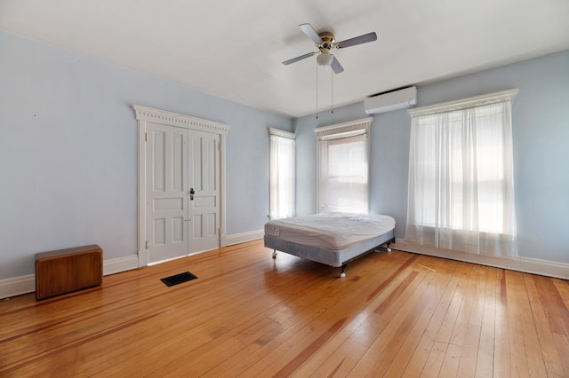 unfurnished bedroom with light hardwood / wood-style flooring, ceiling fan, multiple windows, and a wall mounted air conditioner