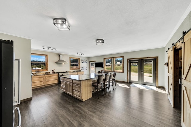 kitchen with a center island, a barn door, dark hardwood / wood-style flooring, track lighting, and wall chimney range hood