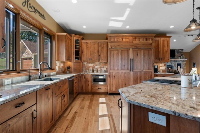 kitchen with light wood-type flooring, stainless steel appliances, sink, a stone fireplace, and pendant lighting