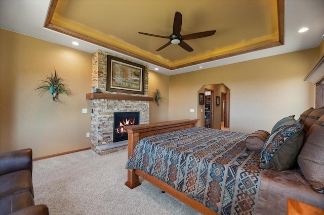 carpeted bedroom featuring a tray ceiling, a fireplace, and ceiling fan