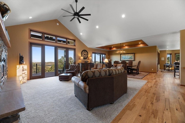 living room featuring ceiling fan with notable chandelier, light wood-type flooring, high vaulted ceiling, and a tray ceiling