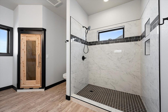 bathroom with hardwood / wood-style flooring, a tile shower, and toilet