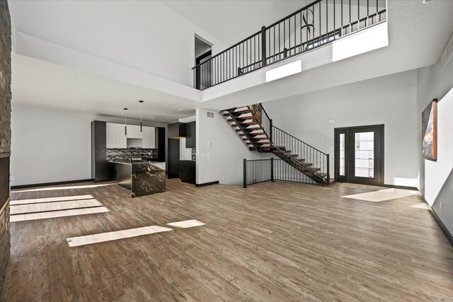 kitchen featuring tasteful backsplash, hanging light fixtures, a kitchen island with sink, stainless steel stove, and light hardwood / wood-style floors