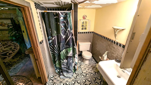 bathroom featuring curtained shower, tile walls, toilet, and sink