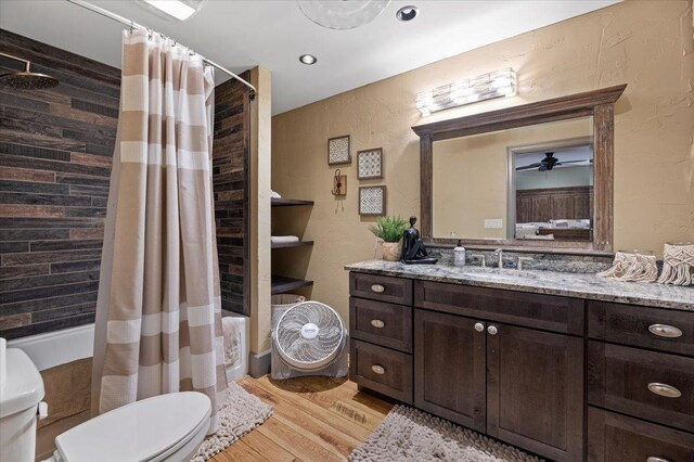 bedroom with a wall mounted air conditioner, light hardwood / wood-style flooring, ensuite bath, and ceiling fan