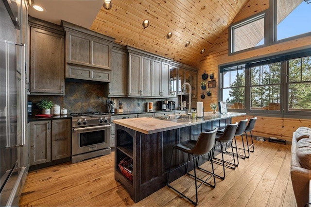 kitchen featuring butcher block counters, light wood-style flooring, an island with sink, high quality appliances, and wooden ceiling