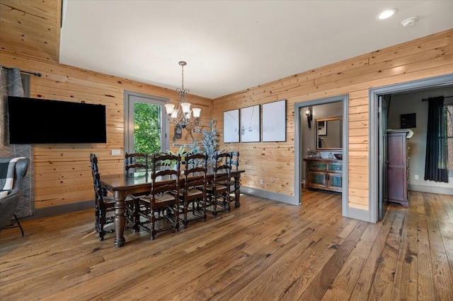 dining space featuring baseboards, wooden walls, an inviting chandelier, and hardwood / wood-style flooring