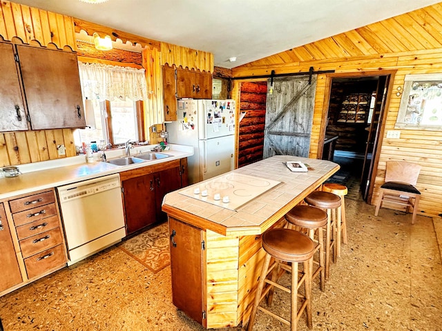 kitchen with a breakfast bar area, white appliances, tile counters, sink, and a barn door