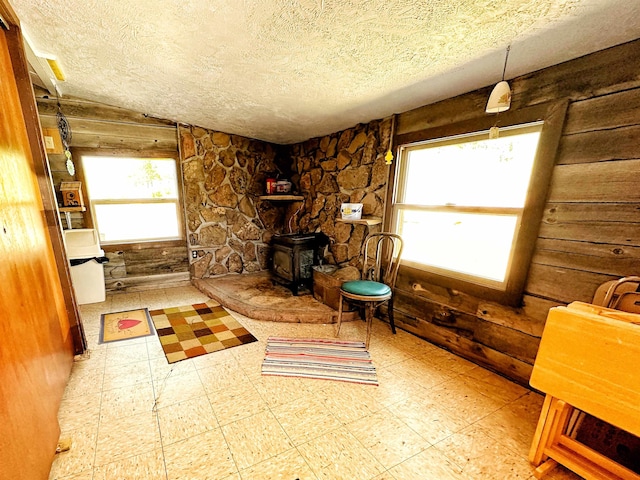 sitting room with a textured ceiling, plenty of natural light, wood walls, and a wood stove