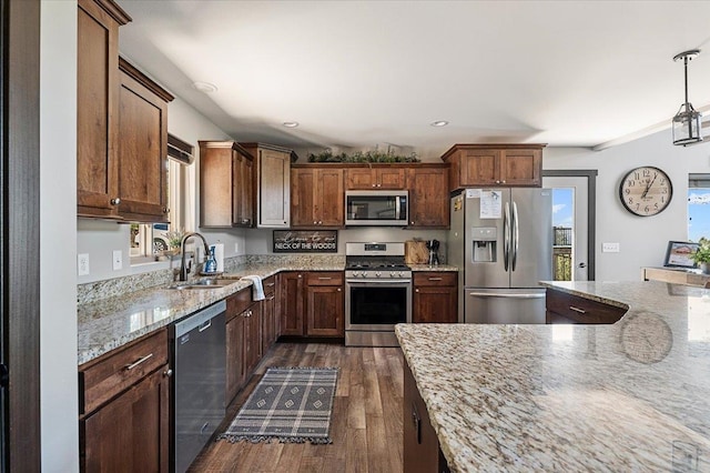 kitchen featuring sink, light stone countertops, hanging light fixtures, dark hardwood / wood-style floors, and appliances with stainless steel finishes