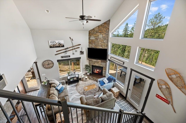 living room with a healthy amount of sunlight, ceiling fan, a stone fireplace, and high vaulted ceiling