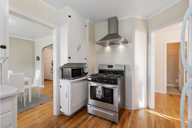 kitchen with wall chimney range hood, stainless steel appliances, light hardwood / wood-style floors, and crown molding