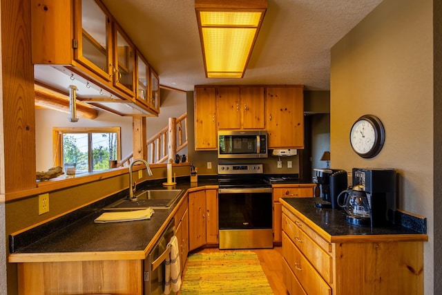 kitchen featuring a peninsula, appliances with stainless steel finishes, a sink, brown cabinets, and light wood finished floors
